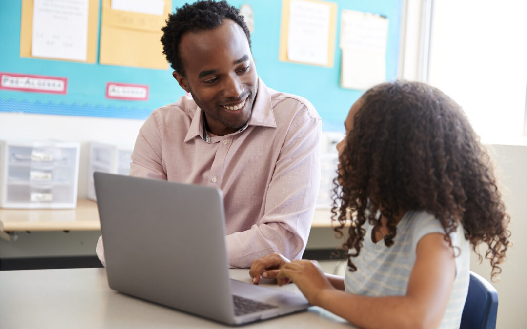 Teacher working with elementary school girl at laptop